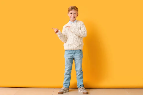 Cute little boy in autumn clothes pointing at something on color wall — Stock Photo, Image