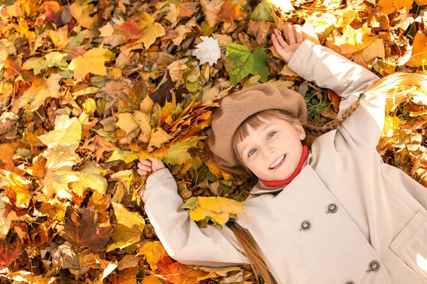 Cute little girl lying on leaves in autumn park — Stock Photo, Image