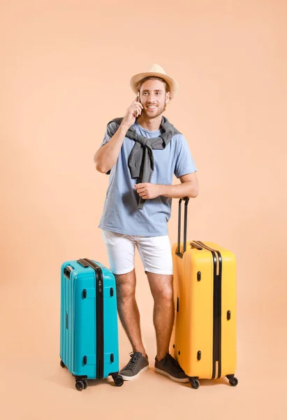 Young tourist with luggage talking by phone on color background — 스톡 사진