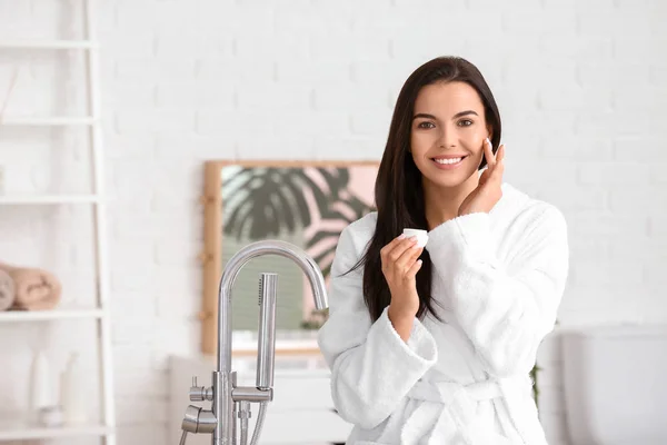 Beautiful young woman applying cream in bathroom — Stock Photo, Image