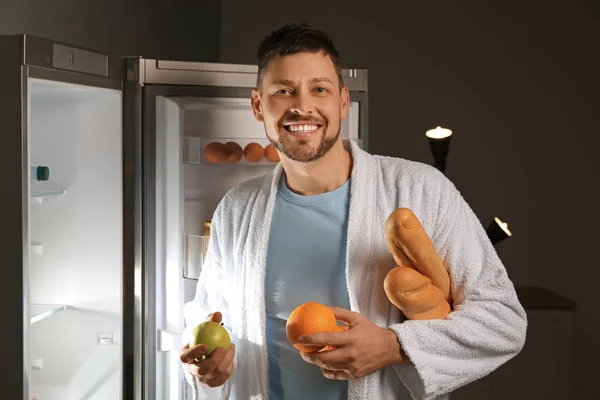 Bonito homem escolhendo comida na geladeira à noite — Fotografia de Stock