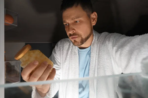 Bonito homem escolhendo comida na geladeira à noite, vista de dentro — Fotografia de Stock