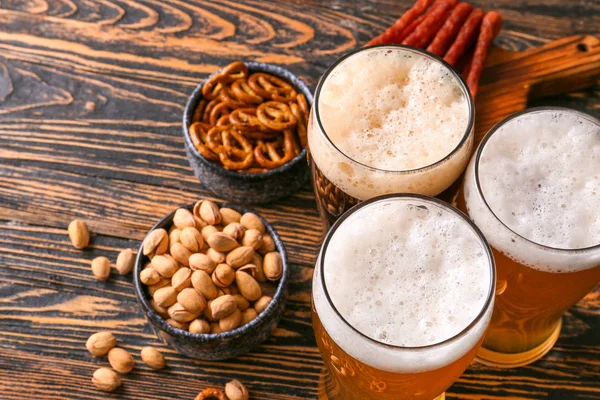 Gläser mit verschiedenen leckeren Bieren mit Snacks auf Holztisch — Stockfoto