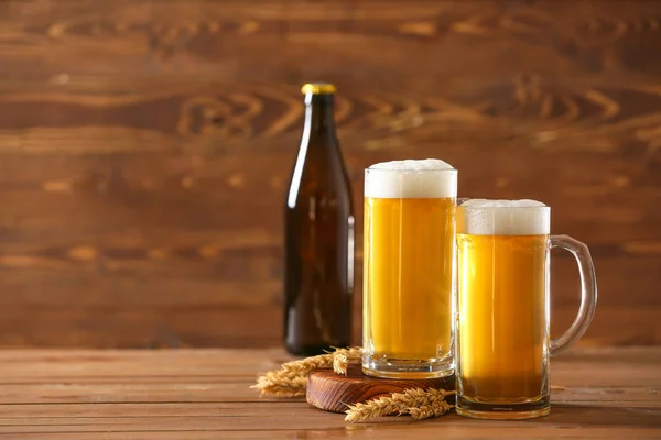 Bottle and mugs of tasty beer on wooden background — Stock Photo, Image