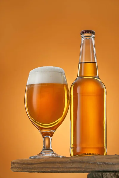Bottle and glass of beer on table against color background — Stock Photo, Image