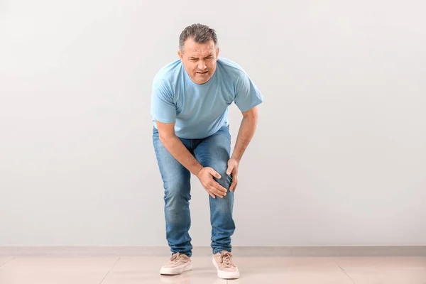 Mature man suffering from pain in knee near wall — Stock Photo, Image