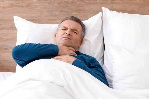 Hombre maduro con dolor de garganta mientras está acostado en la cama —  Fotos de Stock