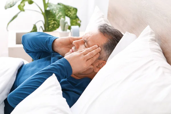 Ώριμος άντρας που υποφέρει από πονοκέφαλο ενώ ξαπλώνει στο κρεβάτι. — Φωτογραφία Αρχείου