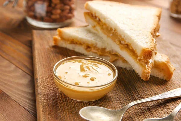 Pão fresco com manteiga de amendoim saborosa na mesa de madeira — Fotografia de Stock