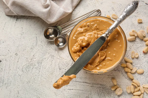 Tigela com manteiga de amendoim saborosa e faca no fundo branco — Fotografia de Stock