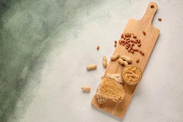 Board with fresh bread and tasty peanut butter on light background — Stock Photo, Image