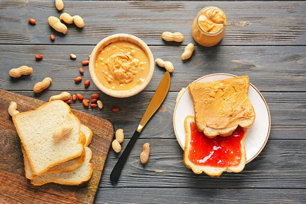 Manteiga de amendoim saborosa em tigela e pão fresco com geléia na mesa de madeira — Fotografia de Stock