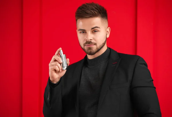 Schöner junger Mann mit einer Flasche Parfüm auf farbigem Hintergrund — Stockfoto