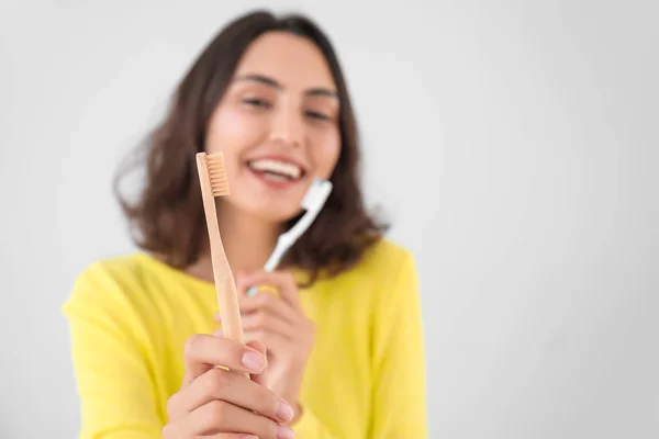 Schöne junge Frau mit verschiedenen Zahnbürsten auf hellem Hintergrund — Stockfoto