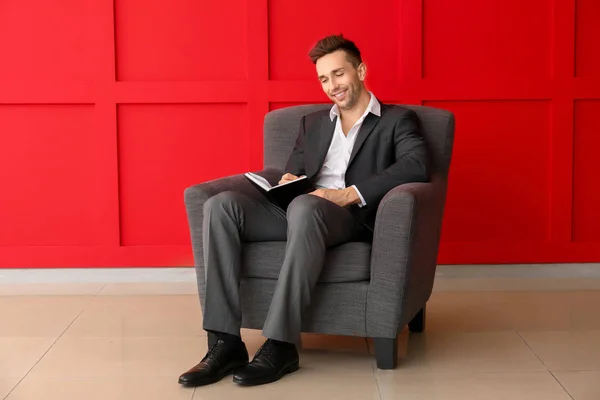 Красивий бізнесмен з блокнотом, що сидить у кріслі біля кольорової стіни — стокове фото