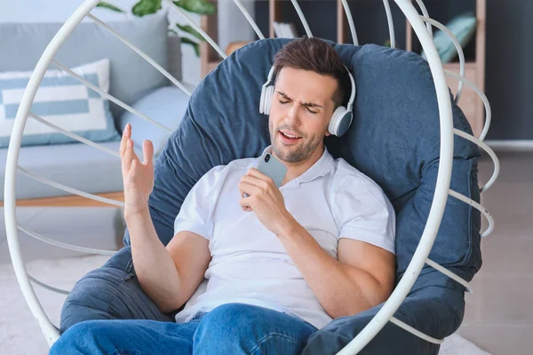 Hombre guapo escuchando música mientras está sentado en el sillón en casa —  Fotos de Stock