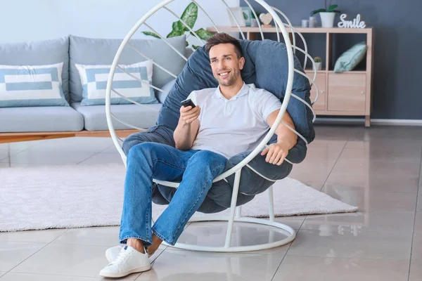 Hombre guapo viendo la televisión mientras está sentado en el sillón en casa — Foto de Stock