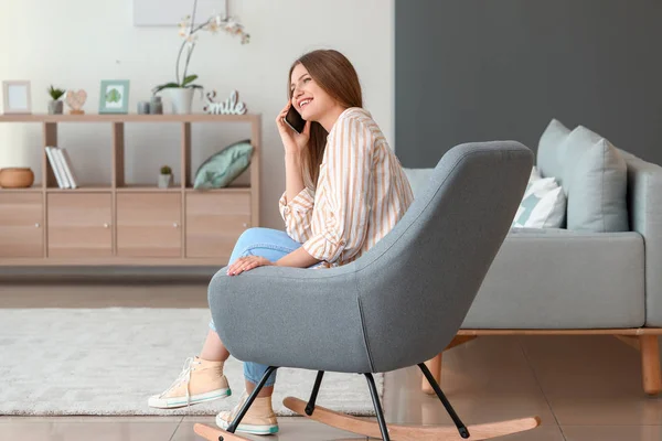 Beautiful woman talking by mobile phone while sitting in armchair at home — Stock Photo, Image