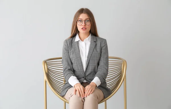 Surprised businesswoman sitting in armchair on light background — Stock Photo, Image