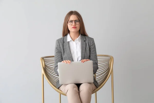 Triste femme d'affaires avec ordinateur portable assis dans un fauteuil sur fond clair — Photo
