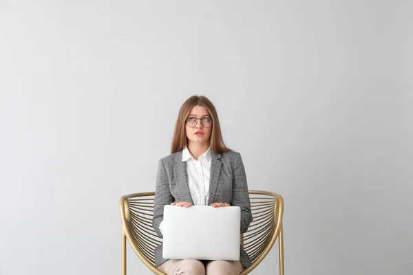 Femme d'affaires réfléchie avec ordinateur portable assis dans un fauteuil sur fond clair — Photo
