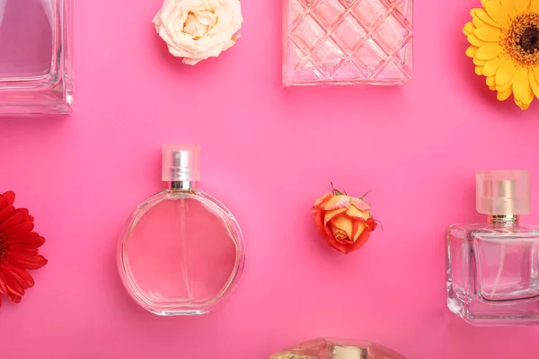 Láhve různých parfémů s květinami na barevném pozadí — Stock fotografie