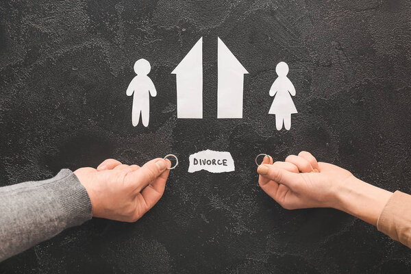 Мужские и женские руки с обручальными кольцами, вырезанные фигуры дома и пара на темном фоне. Концепция развода
