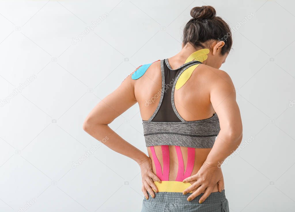 Sporty woman with physio tape applied on back against light background
