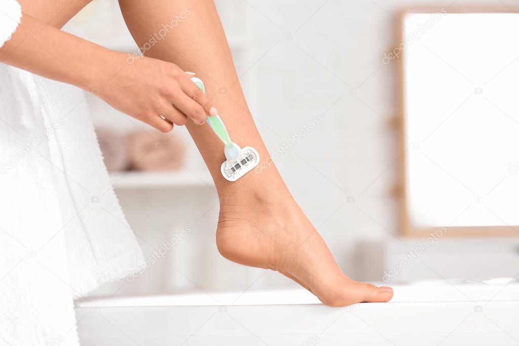 Beautiful young woman shaving legs in bathroom, closeup
