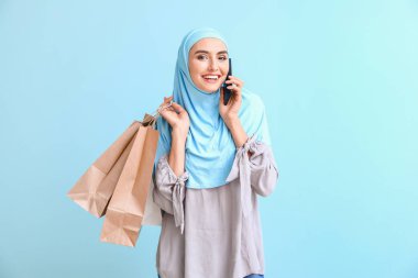 Alışveriş çantalı güzel bir Arap kadın. Arka planda cep telefonuyla konuşuyor.