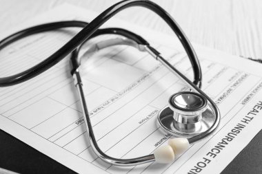 Ahşap arka planda steteskop ve sağlık sigortası formu, yakın plan.