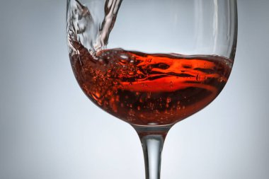 Gri arka planda kadehten şarap dökülüyor, yakın plan.