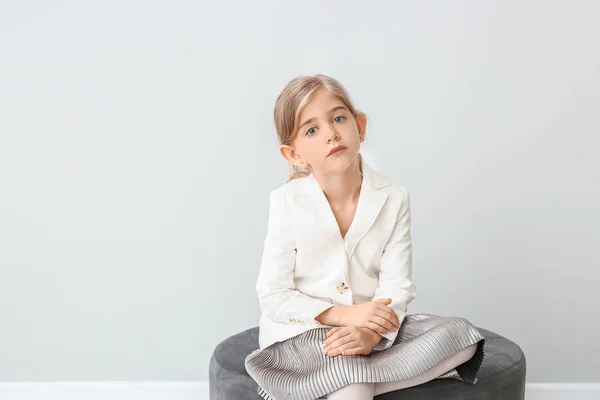 Cute little girl in autumn clothes sitting near grey wall — Stock Photo, Image