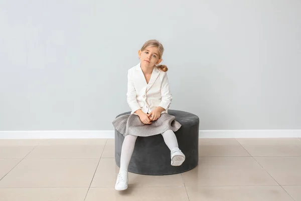 Милая маленькая девочка в осенней одежде сидит возле серой стены — стоковое фото