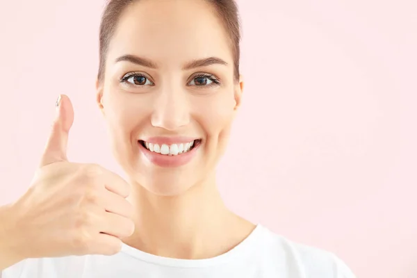 Beautiful young woman with healthy teeth showing thumb-up gesture on color background — Stock Photo, Image