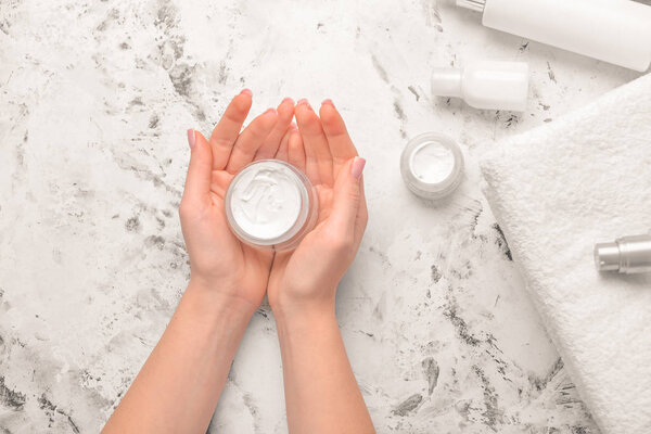 Hands of young woman and cream on white background
