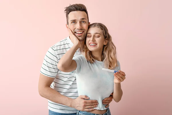 Happy young couple with pregnancy test on color background