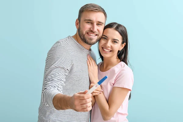 Happy young couple with pregnancy test on color background — Stock Photo, Image