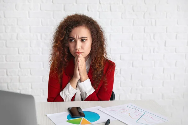 Worried African-American woman at table in office — Stock Photo, Image