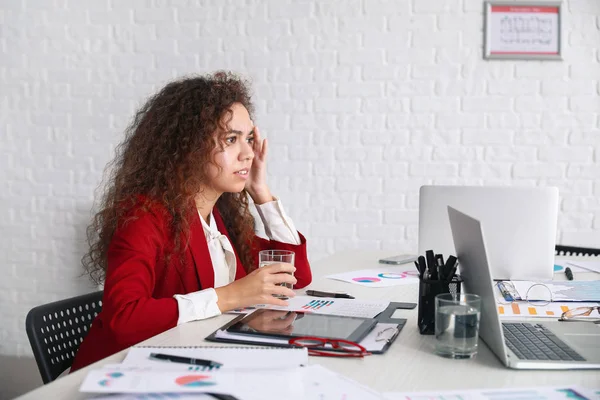 Worried African-American woman at table in office — Stock Photo, Image