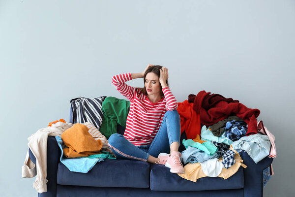 Sad woman with heap of clothes on sofa indoors