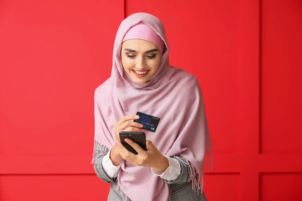 Mulher árabe bonita com telefone celular e cartão de crédito no fundo de cor — Fotografia de Stock