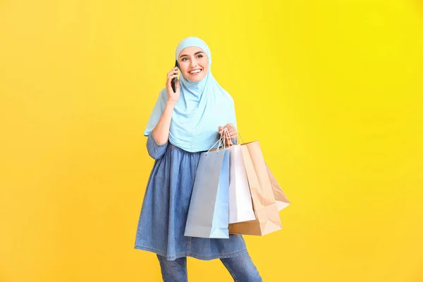 Mulher árabe bonita com sacos de compras falando por telefone celular no fundo de cor — Fotografia de Stock