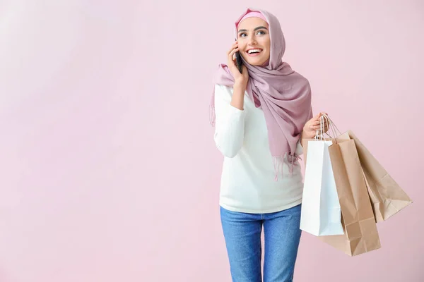 Mujer árabe hermosa con bolsas de compras hablando por teléfono móvil en el fondo de color —  Fotos de Stock
