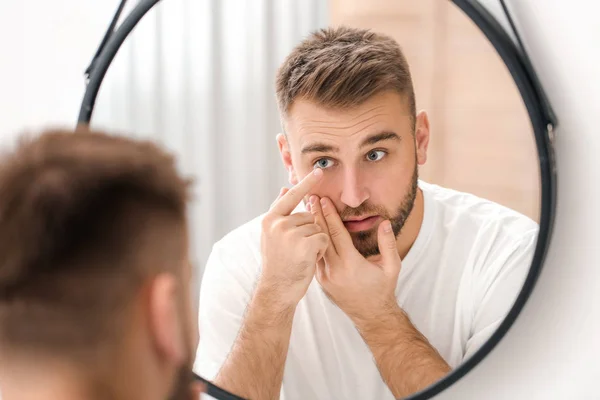 Young man putting in contact lenses near mirror — 스톡 사진