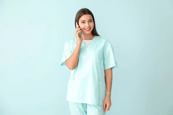 Ung sjuksköterska talar med mobiltelefon på färg bakgrund — Stockfoto