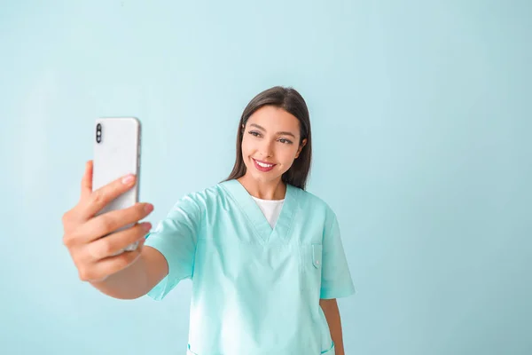 Young nurse taking selfie on color background — Stock Photo, Image