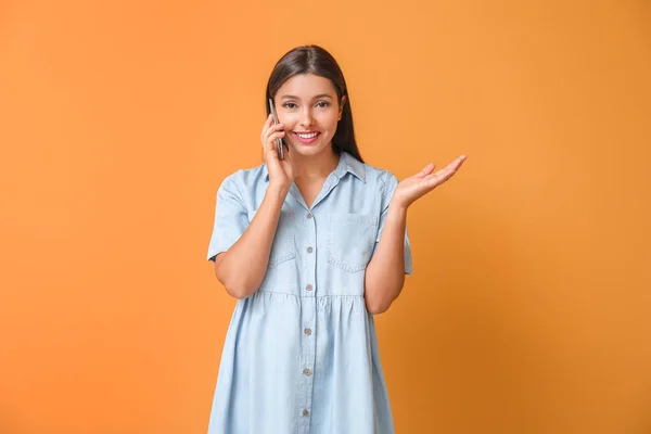 Young woman talking by mobile phone on color background — Stock Photo, Image