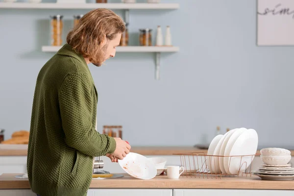 Junger Mann spült Geschirr in Küche — Stockfoto