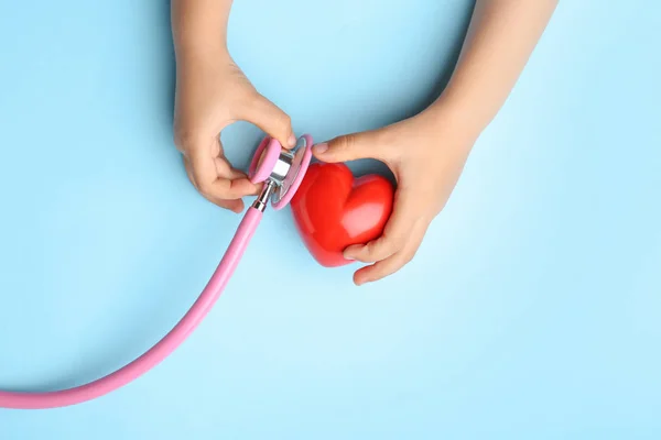 Kinderhände mit rotem Herz und Stethoskop auf farbigem Hintergrund. Kardiologie-Konzept — Stockfoto